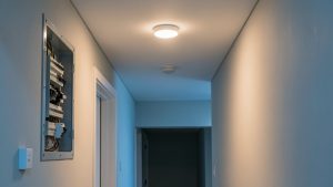 Couloir résidentiel avec une lumière LED à détecteur et un tableau électrique ouvert, montrant un disjoncteur abaissé.