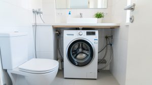 Lave-linge compact installé dans une petite salle de bain, avec les raccordements d’eau facilement accessibles et un espace soigneusement optimisé.