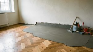 Sol intérieur en rénovation avec une bande irrégulière comblée par un enduit de nivellement pour retrouver la hauteur du parquet existant.